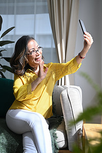 应用视频摄影照片_快乐的老年女性拿着智能手机与朋友或亲戚进行视频通话，享受愉快的交谈