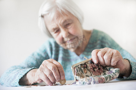 老钱摄影照片_忧心忡忡的老妇人坐在桌旁数着钱包里的钱。