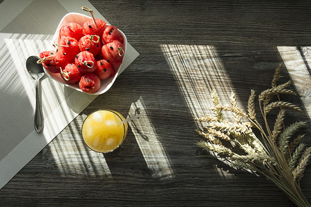 红色穗摄影照片_阳光下的木桌上放着鲜榨橙汁、甜西瓜甜点和成熟小麦的小穗。