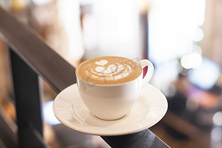 一杯带有拿铁艺术的卡布奇诺咖啡站在散焦的咖啡馆背景上。