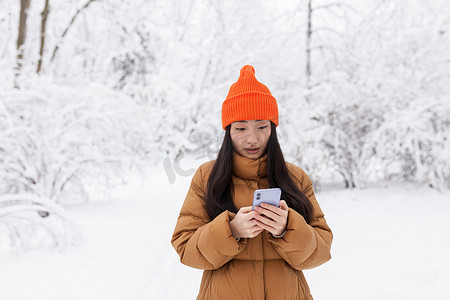 冬天下雪的时候，美丽的亚洲女人在公园里散步，用手机网上购物