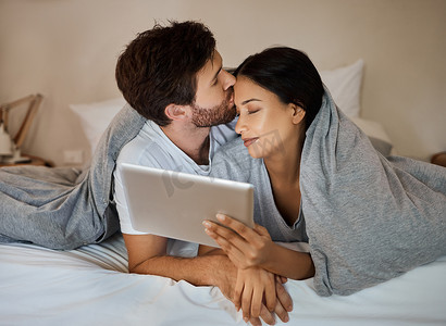 情侣、爱情和平板电脑娱乐，同时躺在床上看电影、浏览互联网和流媒体服务时在额头上亲吻。