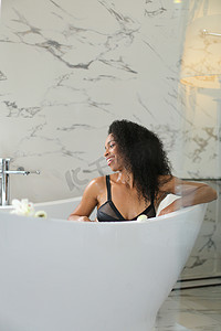 黑人女孩坐在浴缸里，穿着内衣，背景是大理石墙。