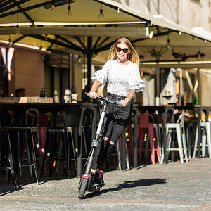 在城市环境中骑着公共租赁电动滑板车的时髦时髦的少女。