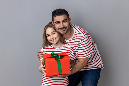 红色3礼盒摄影照片_手拿红色礼盒的积极家庭，父亲和女儿为母亲的生日送礼物
