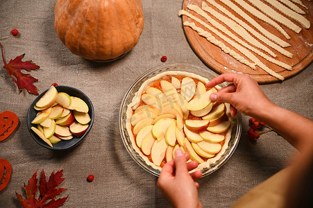 顶视图家庭主妇，糕点师在感恩节那天把苹果片放在生南瓜派上。
