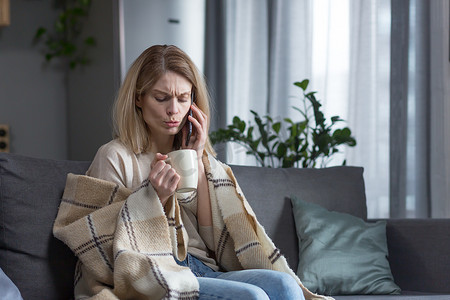家里一个生病而悲伤的女人坐在毯子上，盖着毯子