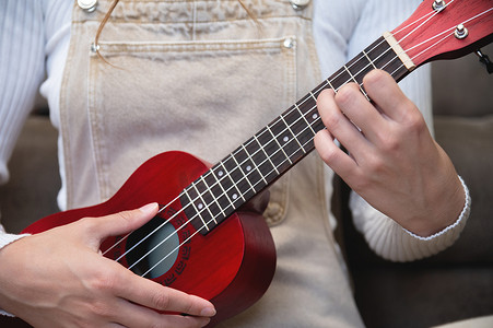 年轻女子在家弹红色尤克里里琴，坐在地板上，打扮成时髦，学习歌曲