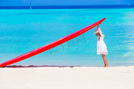 热带白色海滩上有红色大冲浪板的可爱小女孩