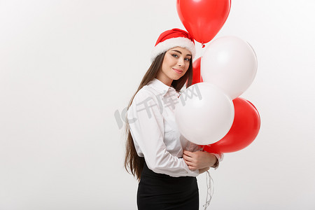 经营理念-美丽年轻自信的女商人拿着圣诞老人的帽子拿着气球庆祝圣诞节。