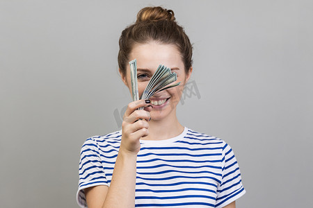 一堆钞票摄影照片_女人穿着条纹 T 恤，偷看一堆美元钞票，被动收入。