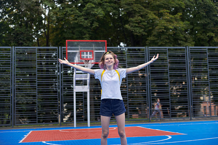街头篮球场上举起双臂活跃微笑的少女