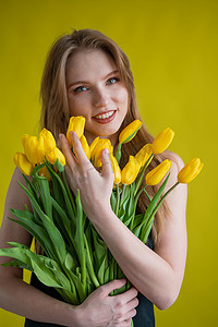 怀抱背景摄影照片_黄色背景上抱着一抱黄色郁金香的白人妇女。