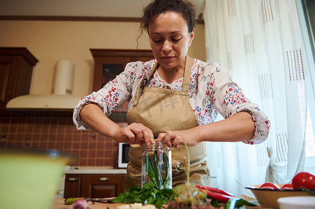 家庭主妇在腌制时令蔬菜时用辣辣椒、切碎的新鲜莳萝叶、大蒜填充罐子
