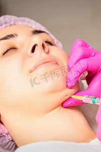 脂肪分解摄影照片_美容师在美容院对一位年轻女子的下巴进行脂肪分解注射，以对抗双下巴。