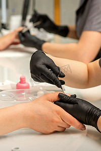 皮肤层摄影照片_美甲师在美甲沙龙中戴着防护手套，用剪刀去除女性指甲上的角质层。