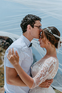 美丽的新娘和新郎在希腊圣托里尼岛的夏季婚礼上在新娘面纱下拥抱和亲吻