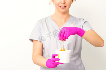 一位白人女性美容师拿着一罐糖膏的肖像，戴着白色背景的粉色手套。
