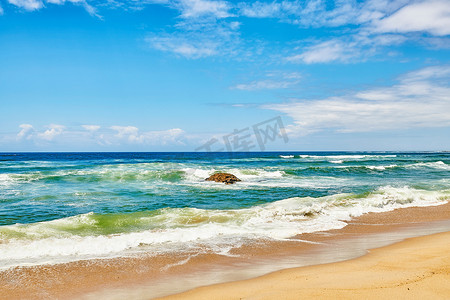 海浪、汹涌的大海和强风带来的汹涌潮汐冲撞在海滩岸边的一块巨石上，蓝天多云复制空间背景。