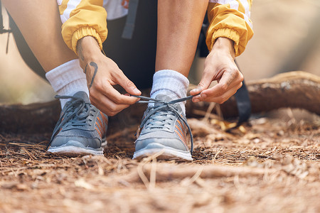 特写照片是一位面目全非的女性在树林里徒步旅行时系上运动鞋的鞋带。不知名的女性在享受周末的森林徒步旅行时确保自己的鞋子和安全