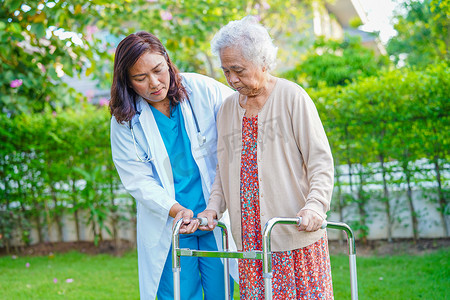 护理人员帮助亚洲老年妇女残疾患者在公园里用步行器行走，这是医疗概念。