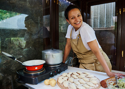 身穿米色厨师围裙的美女在乡村厨房里煮饺子时微笑着看着镜头