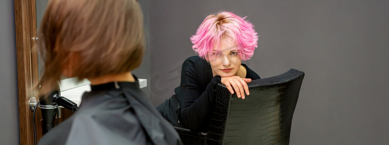 一位美丽的年轻白人女子的肖像，她留着新的粉色短发，坐在美发沙龙的椅子上。