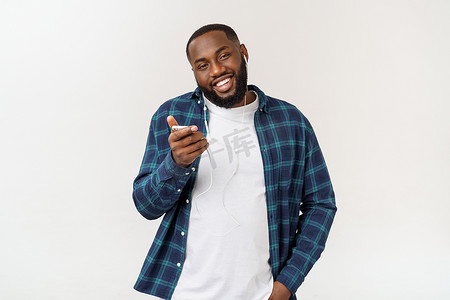 手机听音乐摄影照片_穿着休闲服的英俊的美国黑人男子正在用智能手机听音乐，微笑着。