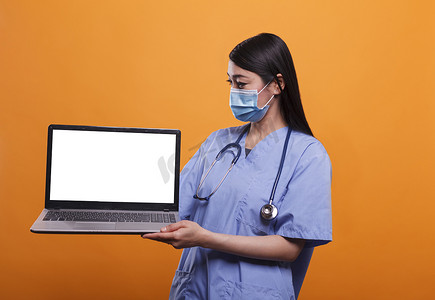 医疗护士戴着面罩和听诊器，同时拿着白屏隔离显示色度键笔记本电脑。