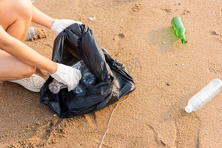 为清洁海滩而将塑料瓶捡进黑色垃圾塑料袋的志愿者妇女