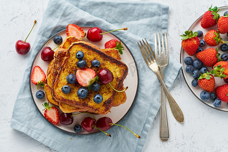 切片水果摄影照片_法式烤面包配浆果、奶油蛋卷早餐、白色背景顶视图