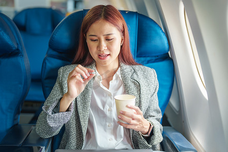 人晕车摄影照片_一位成功的亚洲女商人或企业家在商务舱的飞机上穿着正式西装，在飞行期间服用晕车药的肖像