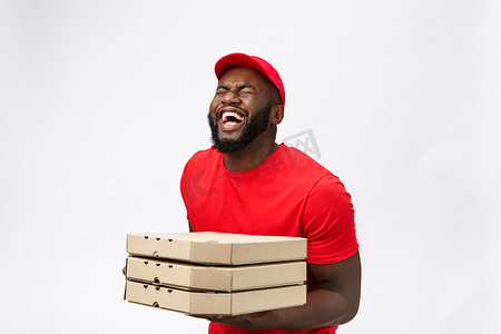 职业照摄影照片_照片中，快乐的非洲裔美国人穿着红色 T 恤和帽子，在送货服务中下订单，拿着白色背景中突显的披萨盒