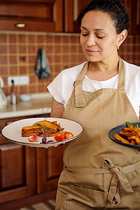 美丽的女人，一位穿着米色厨师围裙的家庭主妇，手里拿着健康的素食餐烤红薯的盘子