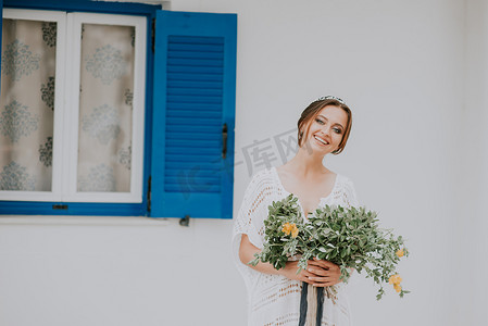 希腊圣托里尼岛白色建筑背景的美丽新娘，蓝窗，是受欢迎的婚礼目的地