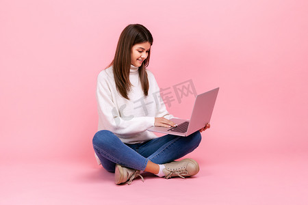 快乐的黑发女孩盘腿坐在地板上，在笔记本电脑上工作，自由职业者的肖像