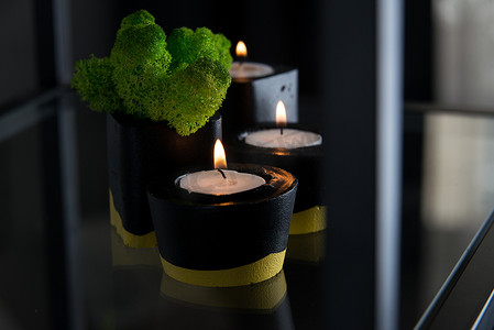 黑色和黄色混凝土烛台中的蜡烛和苔藓