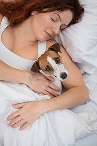 白人妇女抱着她心爱的狗在床上打盹。