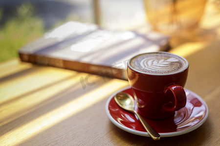 关闭热艺术拿铁咖啡，卡布奇诺咖啡在咖啡店木桌上的红色杯子模糊背景与散景图像。
