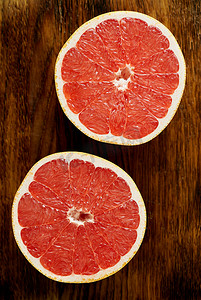 两半红葡萄柚，深色木质背景上的明亮圆圈。