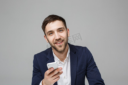 工作玩手机摄影照片_经营理念-肖像英俊快乐英俊的商人穿着西装玩手机，在工作办公室用笔记本电脑微笑。