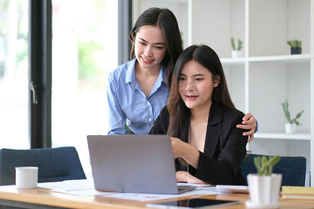 两位年轻的亚洲女商人在办公室讨论新的创业项目创意介绍、分析规划和财务统计以及投资市场。