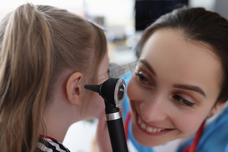 耳鼻喉妇女在诊所用耳镜检查小女孩的耳朵