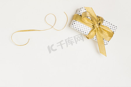 高架视图礼物盒包裹着圆点设计纸，带有闪亮的金色丝带，与白色背景隔离