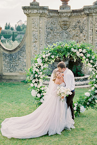 新郎在花园的婚礼拱门亲吻新娘