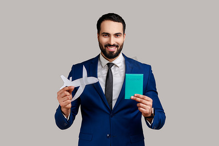 积极高兴的留着胡子的男人微笑着，在镜头前展示护照和纸飞机，旅游。