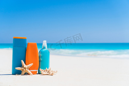 白色沙滩背景海洋上的防晒霜瓶、护目镜、海星