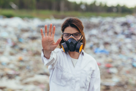 垃圾填埋场一名穿着防护呼吸服的妇女，双手举在前面，试图阻止地球的污染，并用手打出停车标志