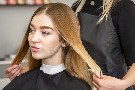 发型设计摄影照片_发型师的手在美容院为女性长发做专业发型设计。