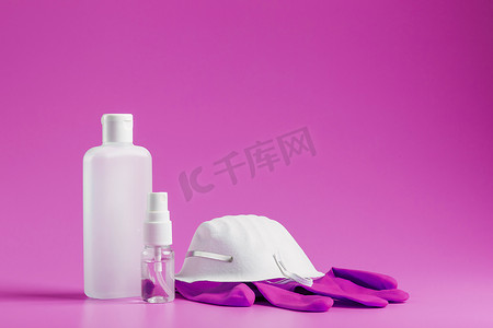 粉红色背景的抗病毒保护套件、面具、橡胶手套、洗手液瓶、抗菌凝胶。